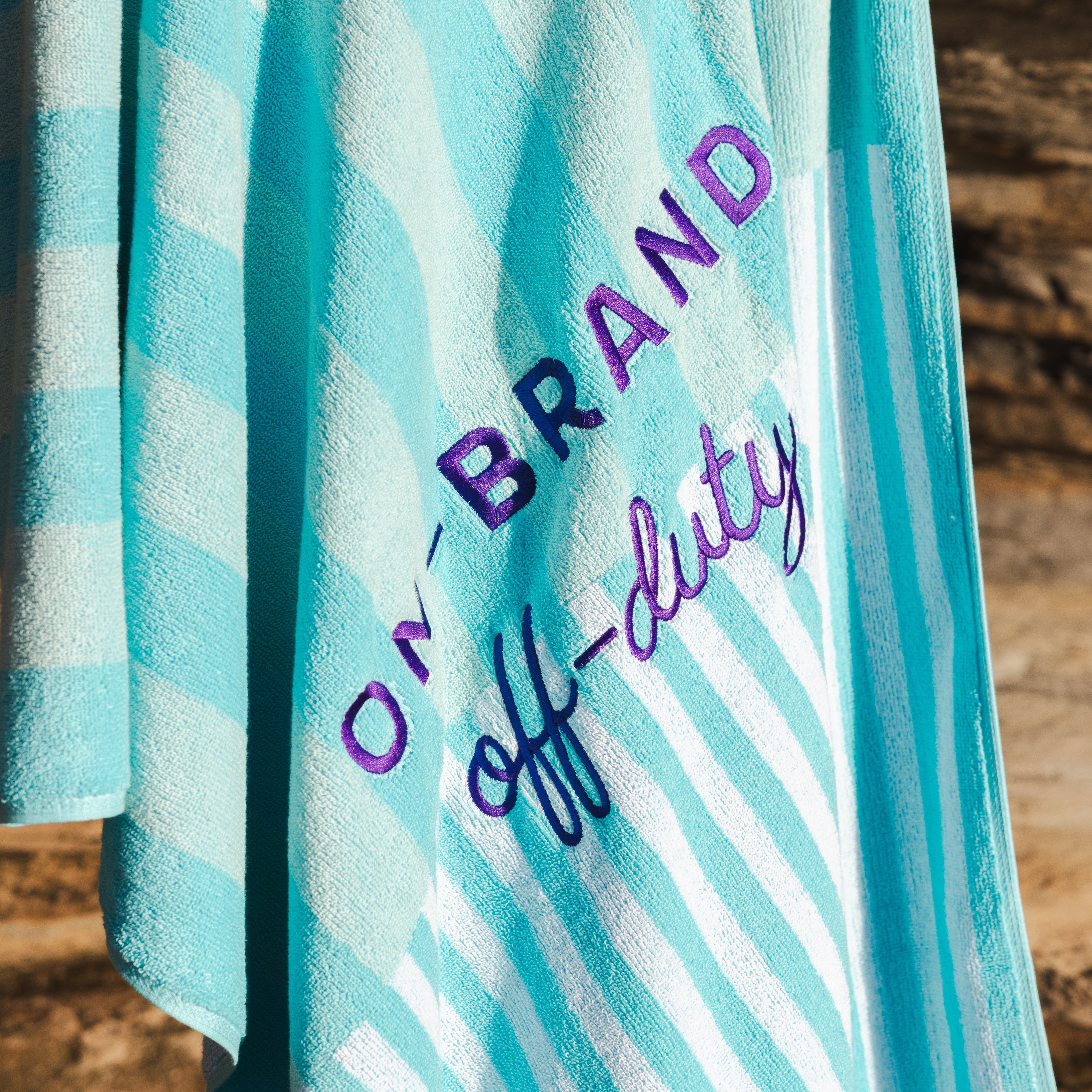 Turquoise and white striped towel with 'OFF-DUTY' text on a wooden surface