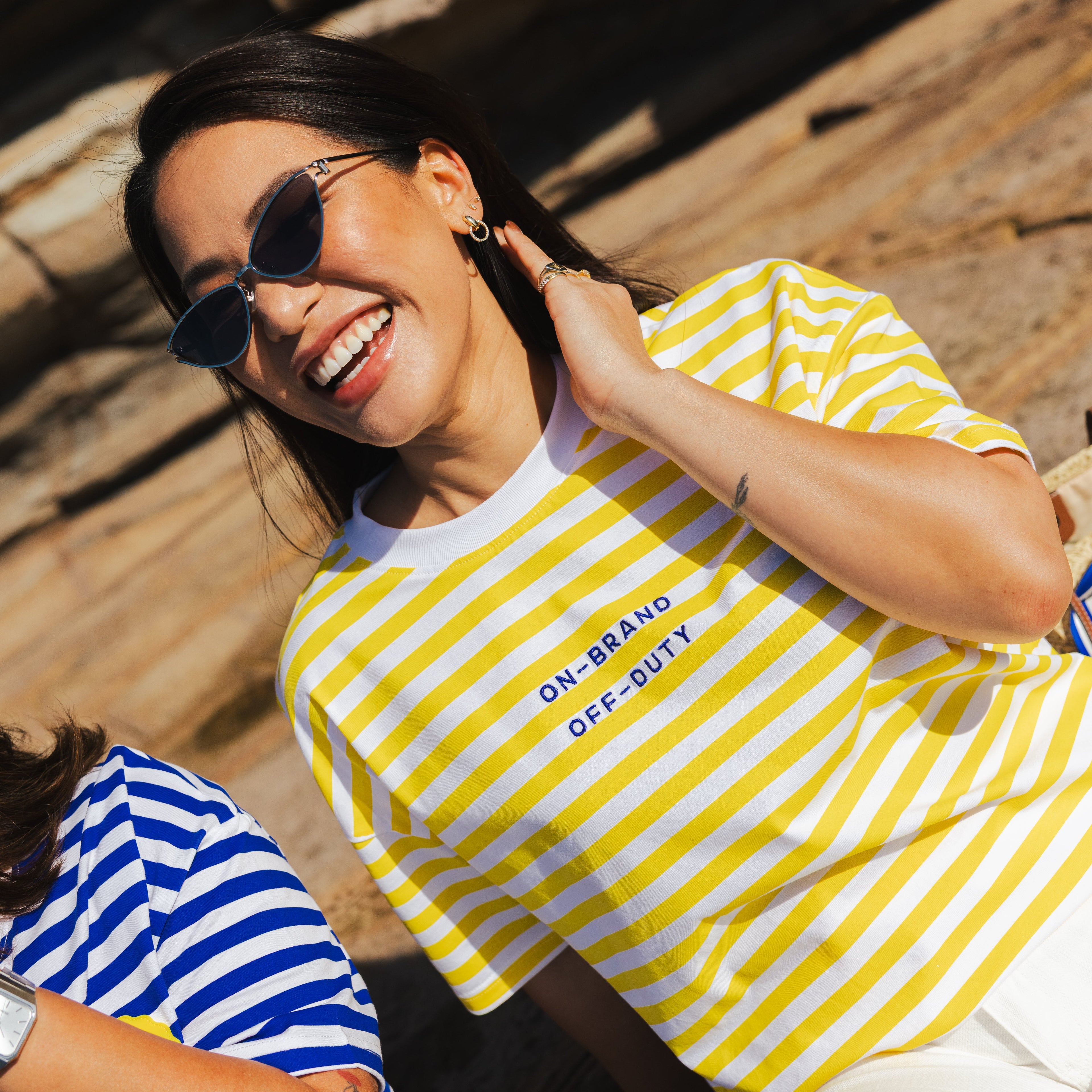 Woman wearing a yellow and white striped shirt with text, sitting outdoors on wooden planks.